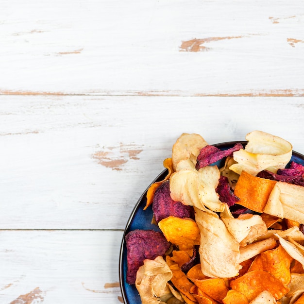 Foto kom met een gezonde snack van groentechips zoals zoete aardappel, biet, pastinaak, wortels.