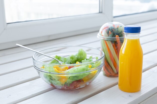 Kom met groene salade, rauwe groenten en een fles sinaasappelsap. Gewichtsverlies, dieet en goed