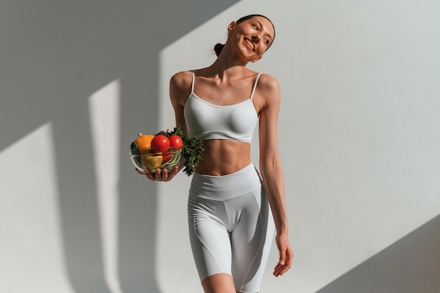 kom met groenten en fruit Jonge blanke vrouw met een slanke lichaamsvorm is binnen in de studio