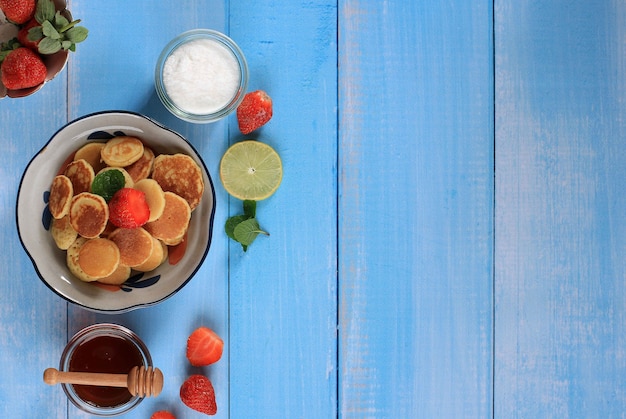 Kom met kleine pannenkoek granen met aardbeien, citroen en muntblaadjes op een blauwe achtergrond. trendy eten. mini cornflakes pannenkoeken. landschap oriëntatie