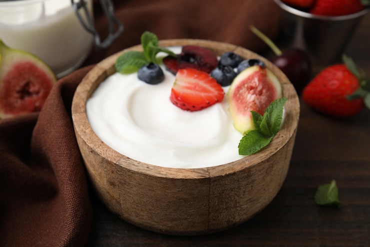 Foto kom met yoghurt, bessen, fruit en munt op een houten tafel.