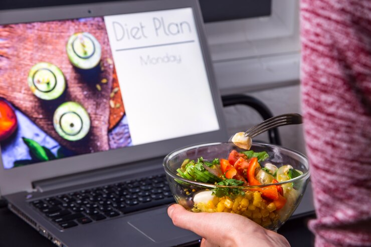 Kom plantaardige salade in vrouwelijke handen dichtbij laptop op de Desktop
