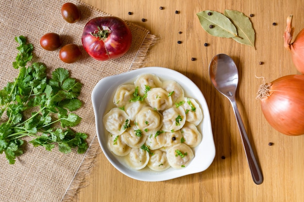 Kom smakelijke dumplings in bouillon, geserveerd op houten tafel, met verse groenten rond. Bovenaanzicht