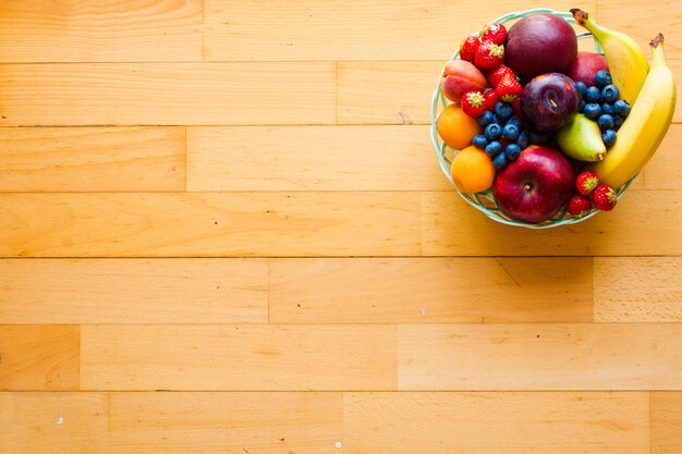 Kom vers fruit met banaan, appel, aardbeien, abrikozen, bosbessen, pruimen, volle granen, vorken, bovenaanzicht