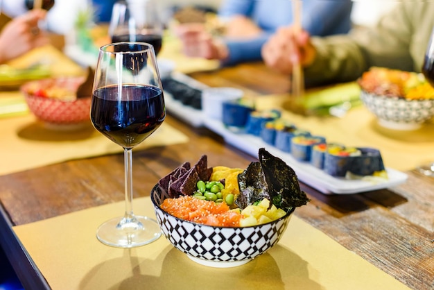 Kom verse Poke en glas rode wijn geserveerd op een restauranttafel met diverse zeevruchten en sushi klaar voor een groep mensen om te eten