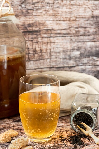 Ферментированный полезный напиток чайного гриба подается в стакане на деревенском столе с ингредиентами