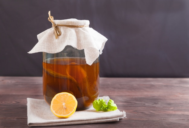 ガラスの瓶に紅茶キノコ、レモン、木製のテーブルにミントの葉。発酵飲料。健康食品のコンセプト。