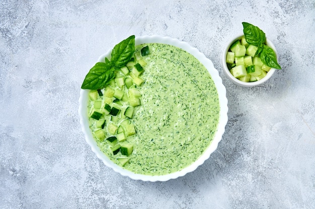 Komkommer gazpacho koude zomersoep met basilicum in witte kom op lichte achtergrond bovenaanzicht plat lag