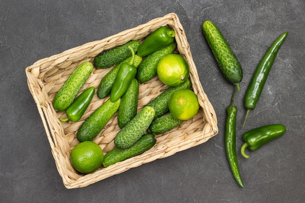 Komkommers, paprika's en limoenen in rotanmand. Groene paprika's op tafel. Zwarte achtergrond. plat leggen