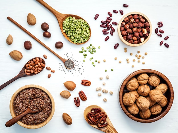 Kommen en lepels van verschillende peulvruchten en verschillende soorten noten op houten tafel.