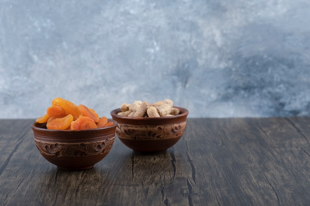 Kommen met gezonde gedroogde abrikozenvruchten en pinda's in de dop op een houten tafel.