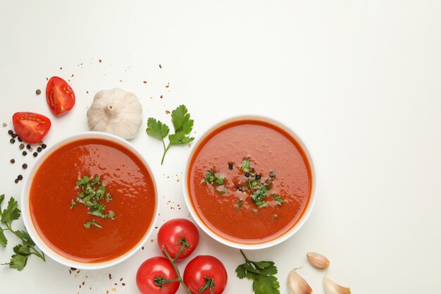 Kommen met tomatensoep en ingrediënten op wit