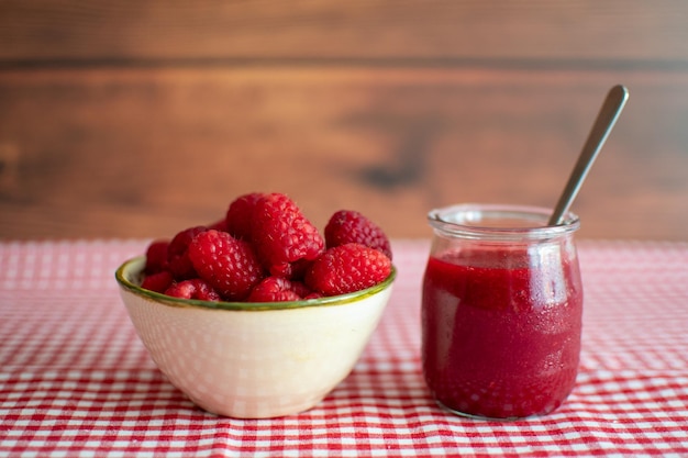 Kommetje met verse frambozen naast een glas met frambozenjam