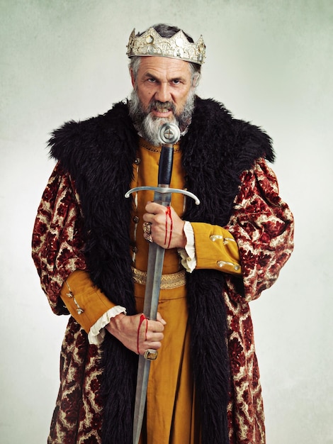 Koning boos en portret van man met zwaard in studio geïsoleerd op een grijze achtergrond