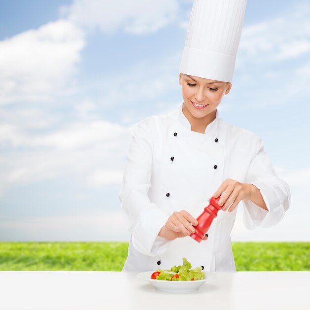 kook- en voedselconcept - glimlachende vrouwelijke chef-kok bereidt salade met zout- of pepermolen