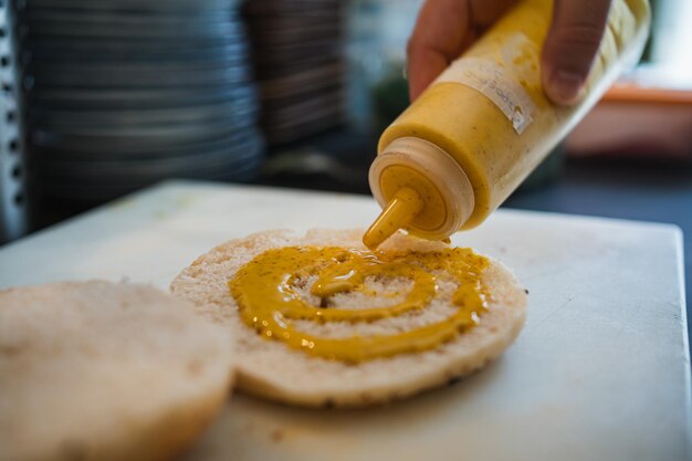 Kook het toevoegen van mosterdsaus aan een bagelbroodje voor de bereiding van een brunch in een café