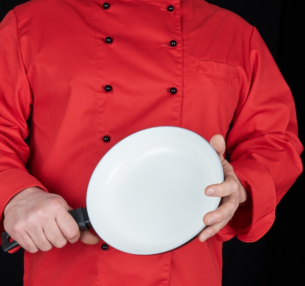 Kook in rood uniform met een lege ronde witte koekenpan
