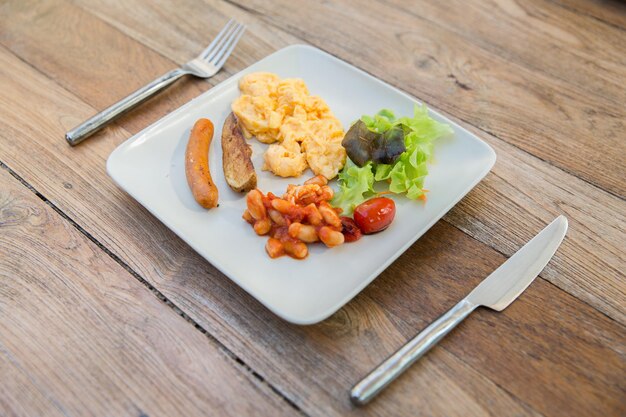 Kook-, keuken- en voedselconcept - bord met worst, eieren, bonen en garnituur op houten tafel in restaurant