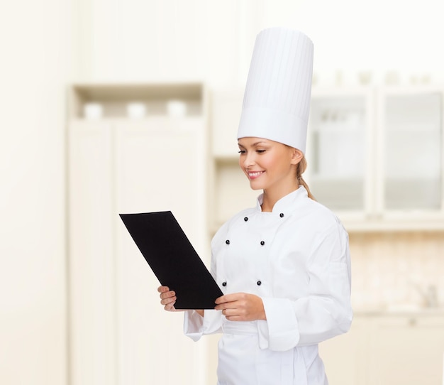kook-, reclame- en voedselconcept - glimlachende vrouwelijke chef-kok met blanco zwart papier