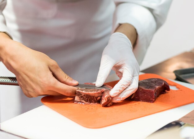 Kook snijdt vers rauw vlees met een mes in de keuken Kook snijden rundvlees op een plank