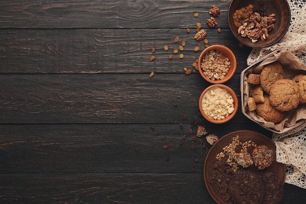 Kookingrediënten voor zelfgemaakte havermoutkoekjes. Havervlokken, noten en rozijnen in houten kommen op donkere rustieke achtergrond met kopieerruimte, bovenaanzicht. Handgemaakt pastei en smakelijk hobbyconcept