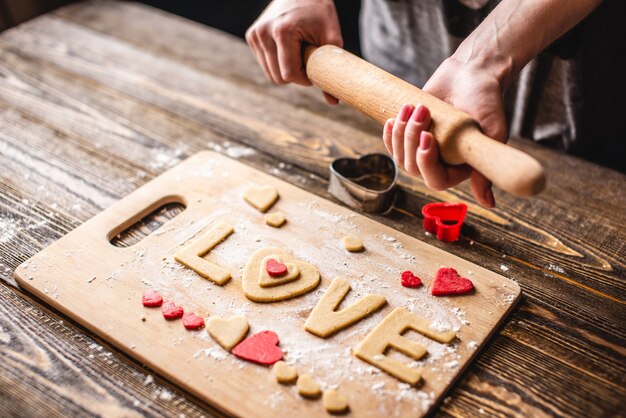 Kookkoekjes van het deeg in de vorm van een hart en het woord liefde op donkere houten achtergrond