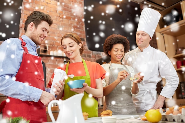 kookles, culinair, bakkerij, eten en mensenconcept - gelukkige groep vrienden en mannelijke chef-kok bakken in de keuken over sneeuweffect