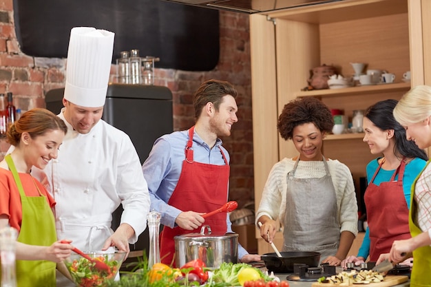 kookles, culinair, eten en mensen concept - gelukkige groep vrienden en mannelijke chef-kok koken in de keuken