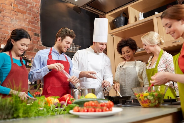 kookles, culinair, eten en mensen concept - gelukkige groep vrienden en mannelijke chef-kok koken in de keuken