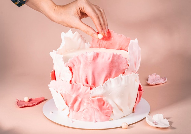 Kookproces Vrouwenhanden versieren cake met witte parel marsepein kralen op roze achtergrond