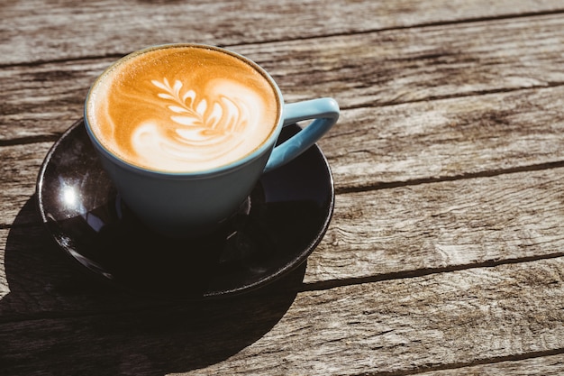 Kop cappuccino met koffiekunst op houten lijst bij koffiewinkel