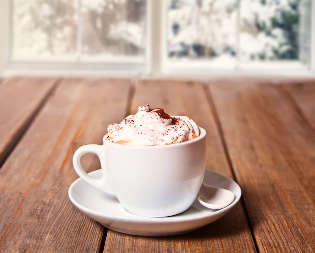 Kop cappuccino op het houten lijst nabijgelegen bevroren venster