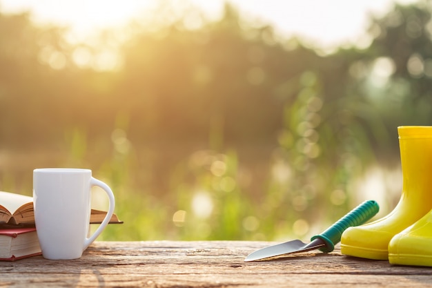 Kop koffie, boek, en tuinmateriaal op houten lijst met zonlicht in ochtendtijd