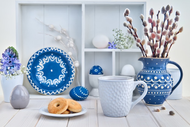 Kop koffie en koekjes op witte lijst met bos van pussy-wilg in blauwe ceramische pot