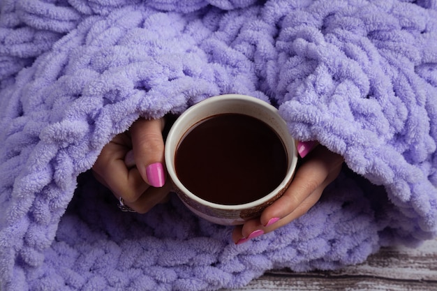 Kop warme chocolademelk in de armen van de vrouw op gebreide plaid. Zelfgemaakte gebreide plaids voor gezellige tijd in de winter thuis.