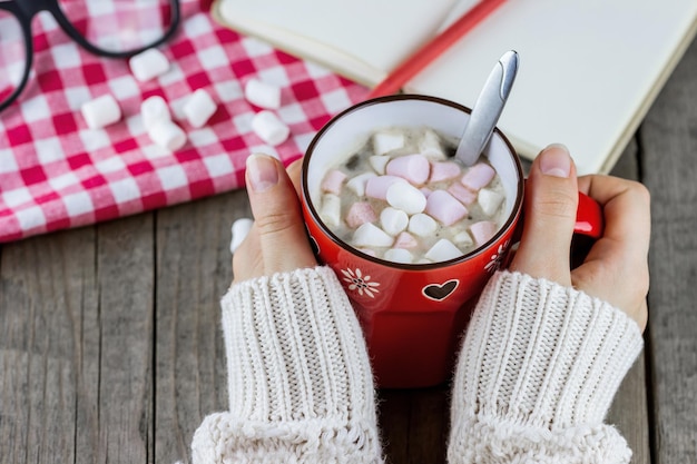 Kop warme chocolademelk met marshmallows in handen op tafel