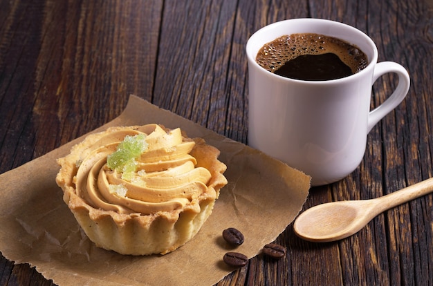 Kop warme koffie en cake met room en marmelade op oude houten tafel