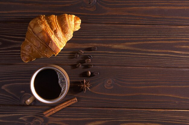 Kop warme koffie en een croissant bij het ontbijt op donkere houten tafel