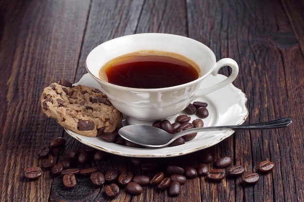 Kop warme koffie en koekje met chocolade op donkere houten tafel