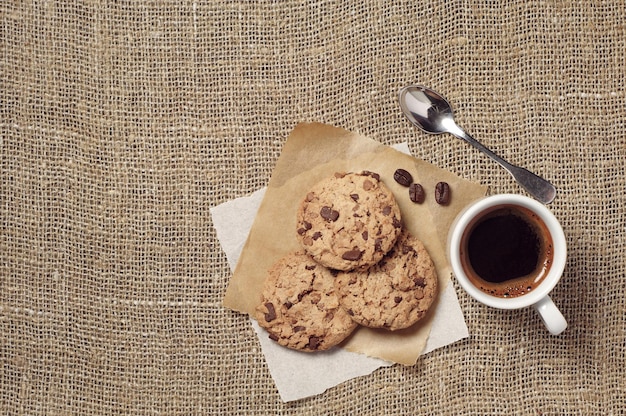 Kop warme koffie en koekjes met chocolade op jute achtergrond, bovenaanzicht