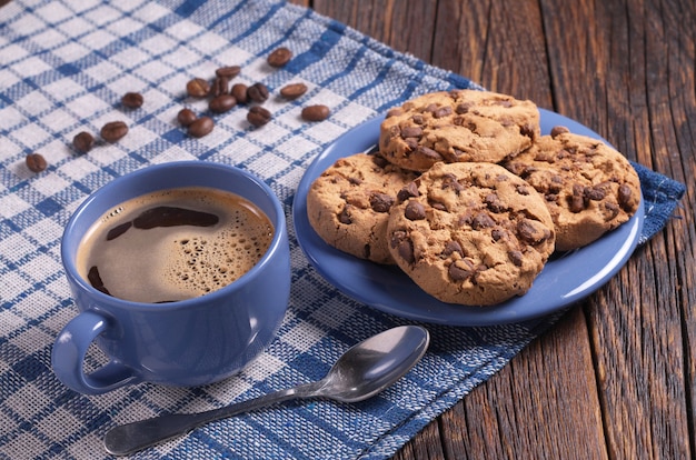 Kop warme koffie en koekjes met chocolade voor het ontbijt op rustieke houten tafel. Blauw servies en tafelkleed