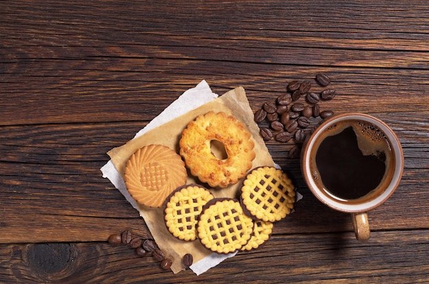 Kop warme koffie en verschillende koekjes op donkere houten tafel, bovenaanzicht