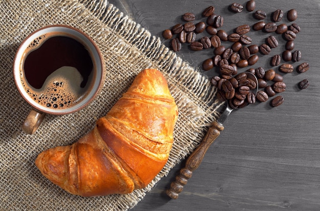 Kop warme koffie en verse croissants op donkere houten tafel, bovenaanzicht