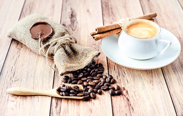 Kop warme koffie kaneelstokjes en koffiebonen in een houten lepel en morsen uit een jutezak op houten rustieke tafel