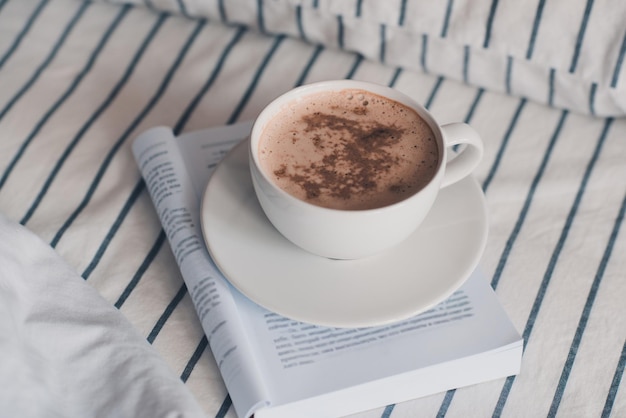 Kop warme koffie met chocolade bovenop, verblijf op papieren boek in bed close-up. goedemorgen. ontbijt.