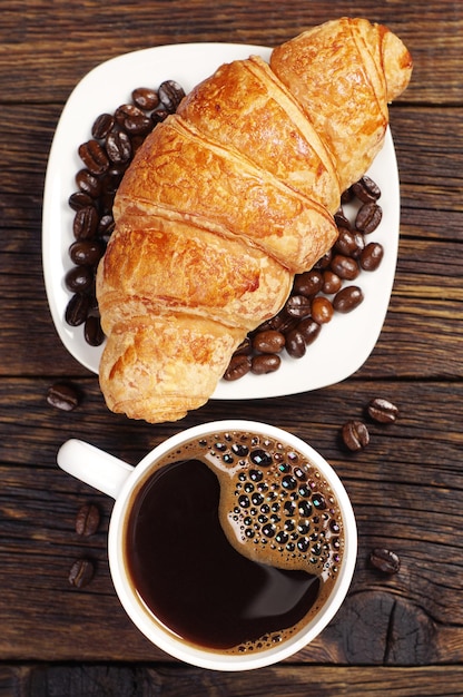 Kop warme koffie met croissant voor het ontbijt op een donkere houten tafel, bovenaanzicht