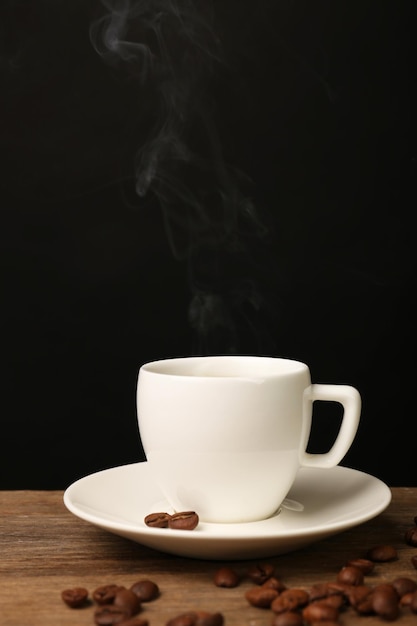 Kop warme koffie met schotel op houten tafel op zwarte achtergrond