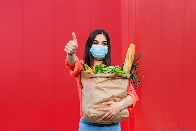 Koper draagt een beschermend masker. Winkelen tijdens de Covid 19, Coronavirus pandemische quarantaine. Vrouw in medische masker houdt een papieren zak met voedsel, fruit en groenten