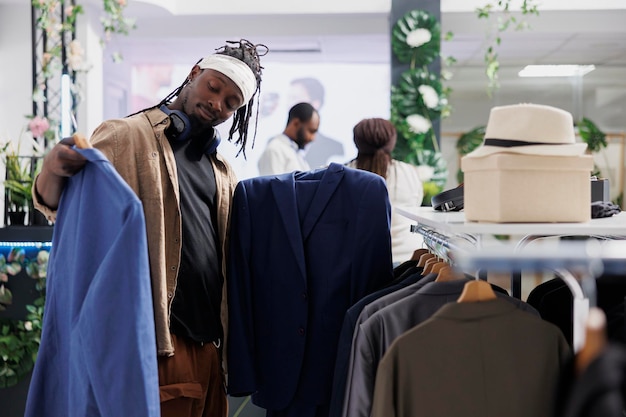 Koper kiest tussen twee jassen tijdens het kiezen van formele kleding in kledingwinkel. Afro-amerikaanse man met blazers op hangers terwijl hij stijl en stof onderzoekt in winkelcentrum