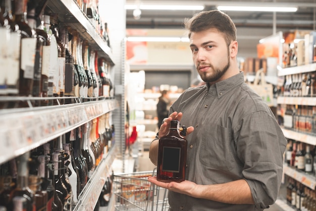 Koper man die zich voordeed op de camera met sterke drank fles in het gangpad van de supermarkt